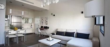 A modern living room with a white sofa, a coffee table, and a dining area with a white table and chairs.