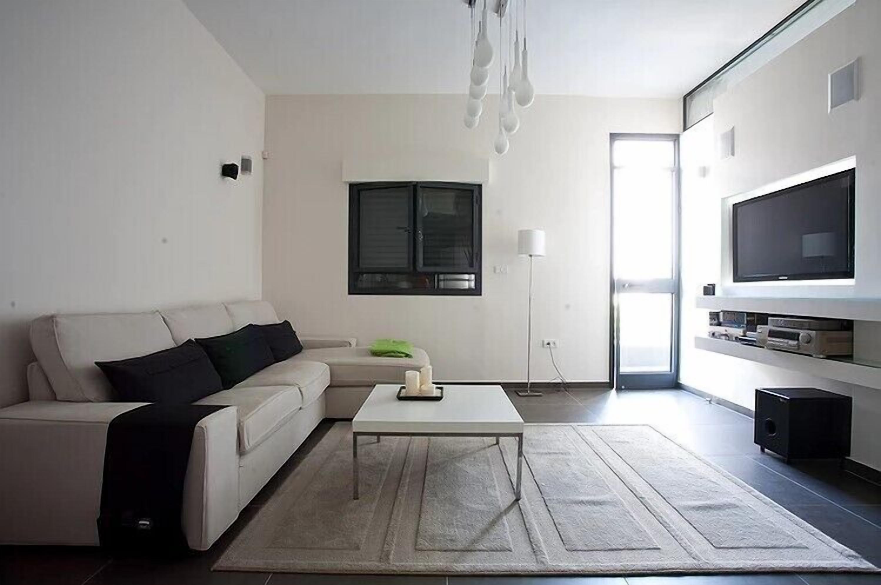 A modern living room with a white sofa, a coffee table, a flat-screen TV, and a large window.