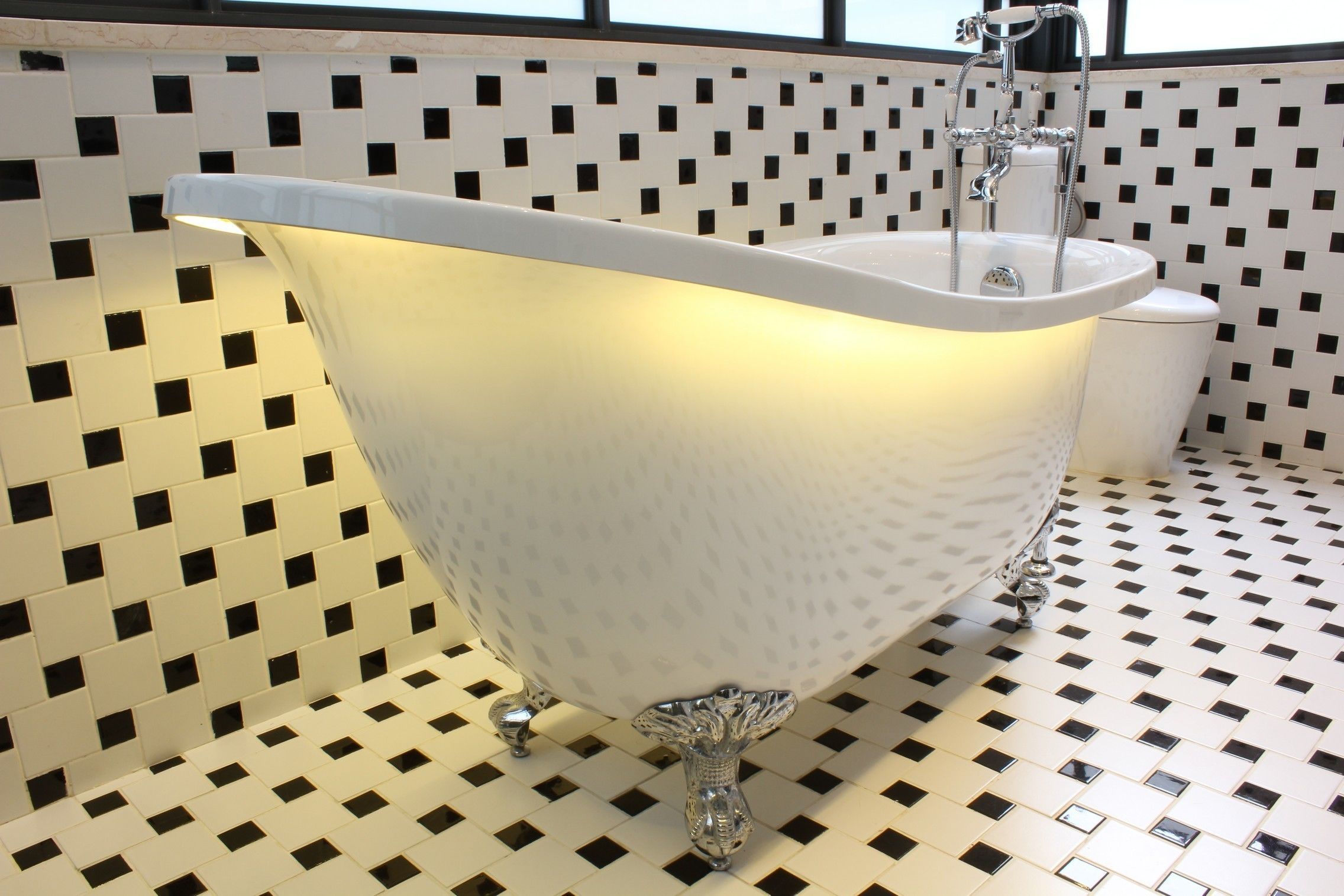A white bathtub with a modern design, set against a tiled wall with a black and white pattern.