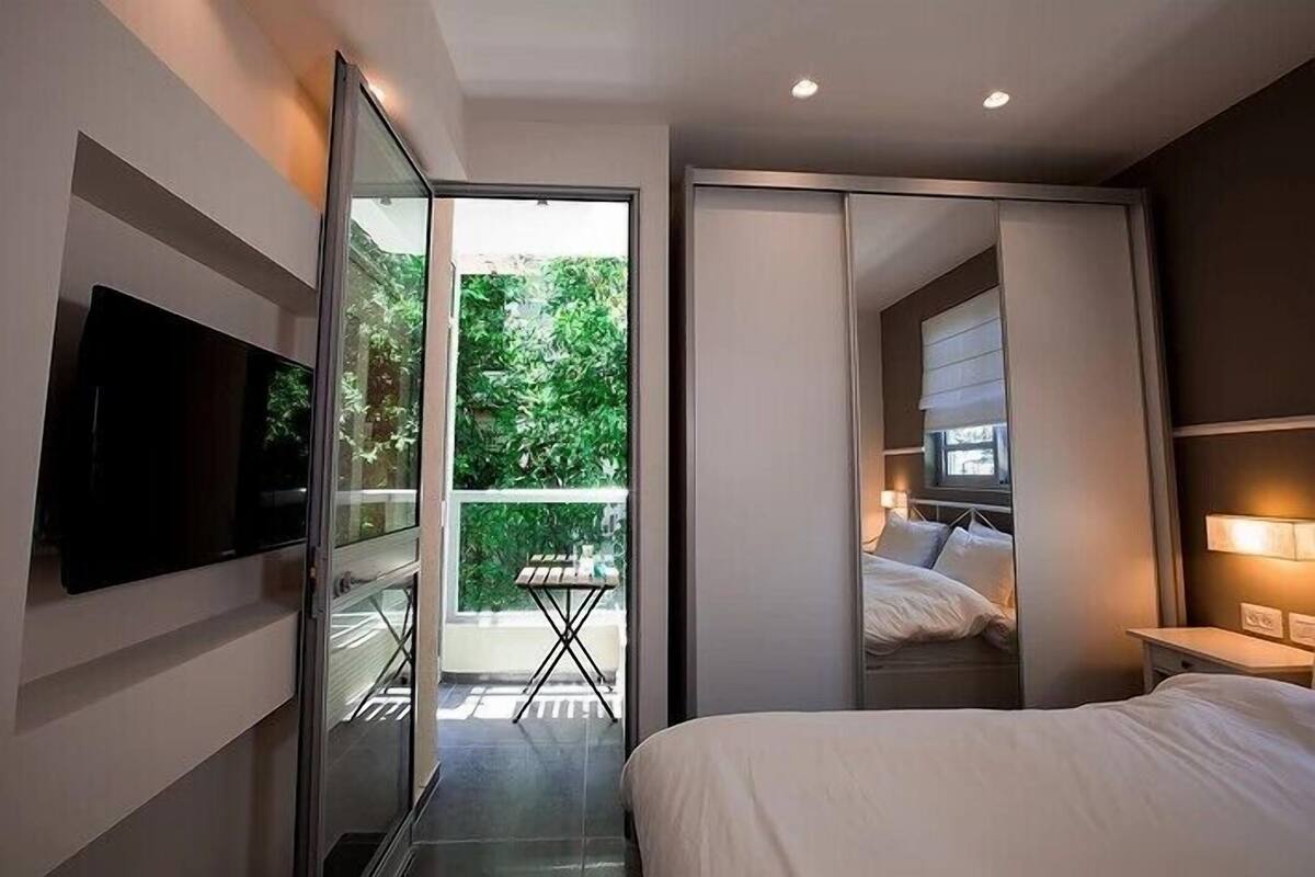 Una habitación de hotel moderna con cama, televisión, balcón con mesa y puerta corredera que da a otra habitación.