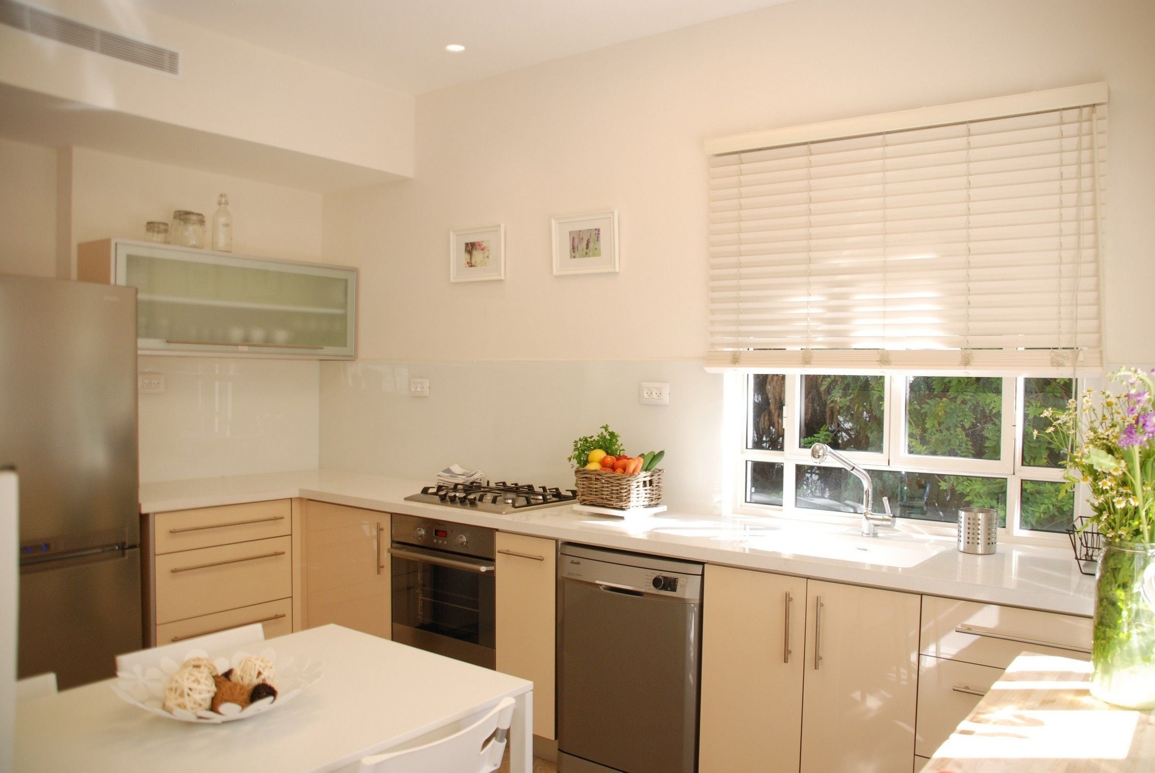Cocina moderna con estufa a gas, horno y lavavajillas, cubierta de encimera blanca y ventana con persianas.