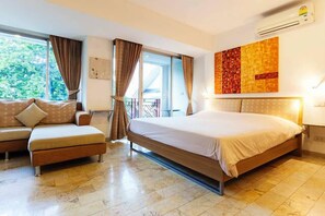 A hotel room with a bed, a sofa, a window with curtains, a balcony, and a wall-mounted air conditioner. - Galare Thong Tower (Chiang Mai)