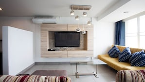 Una sala de estar moderna con un televisor de pantalla plana montado en una pared de madera, una mesa de centro de vidrio, un sofá con cojines estampados y un reposapiés a rayas.