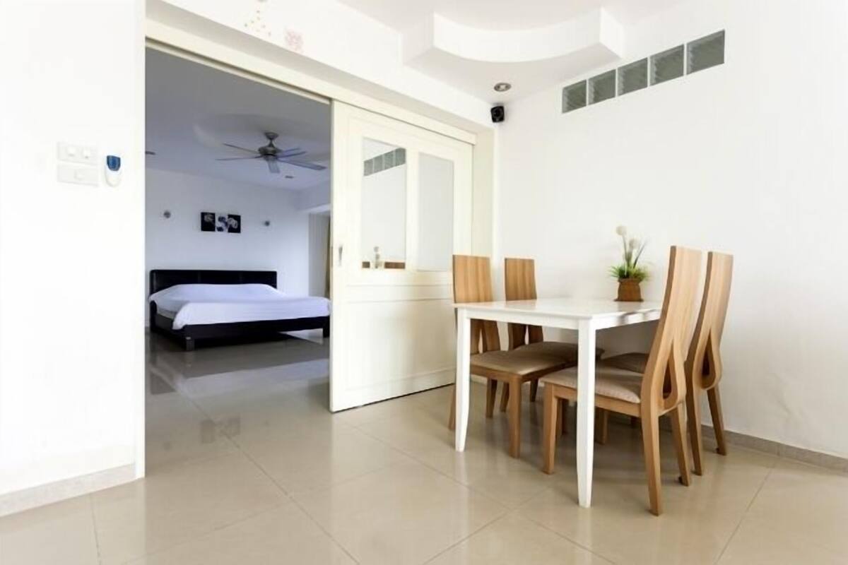 Habitación de hotel con cama, una mesa de comedor con sillas, un ventilador de techo y una pequeña planta en maceta.