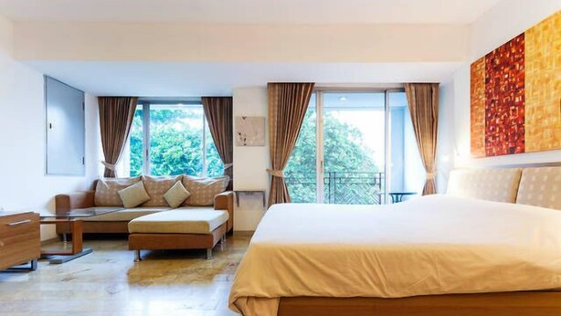 Habitación de hotel moderna con una cama grande, un sofá, una mesita y vistas a zonas verdes por las ventanas.