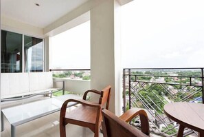 A balcony with a white table and chairs, a glass door, and a view of a cityscape. - Galare Thong Tower (Chiang Mai)
