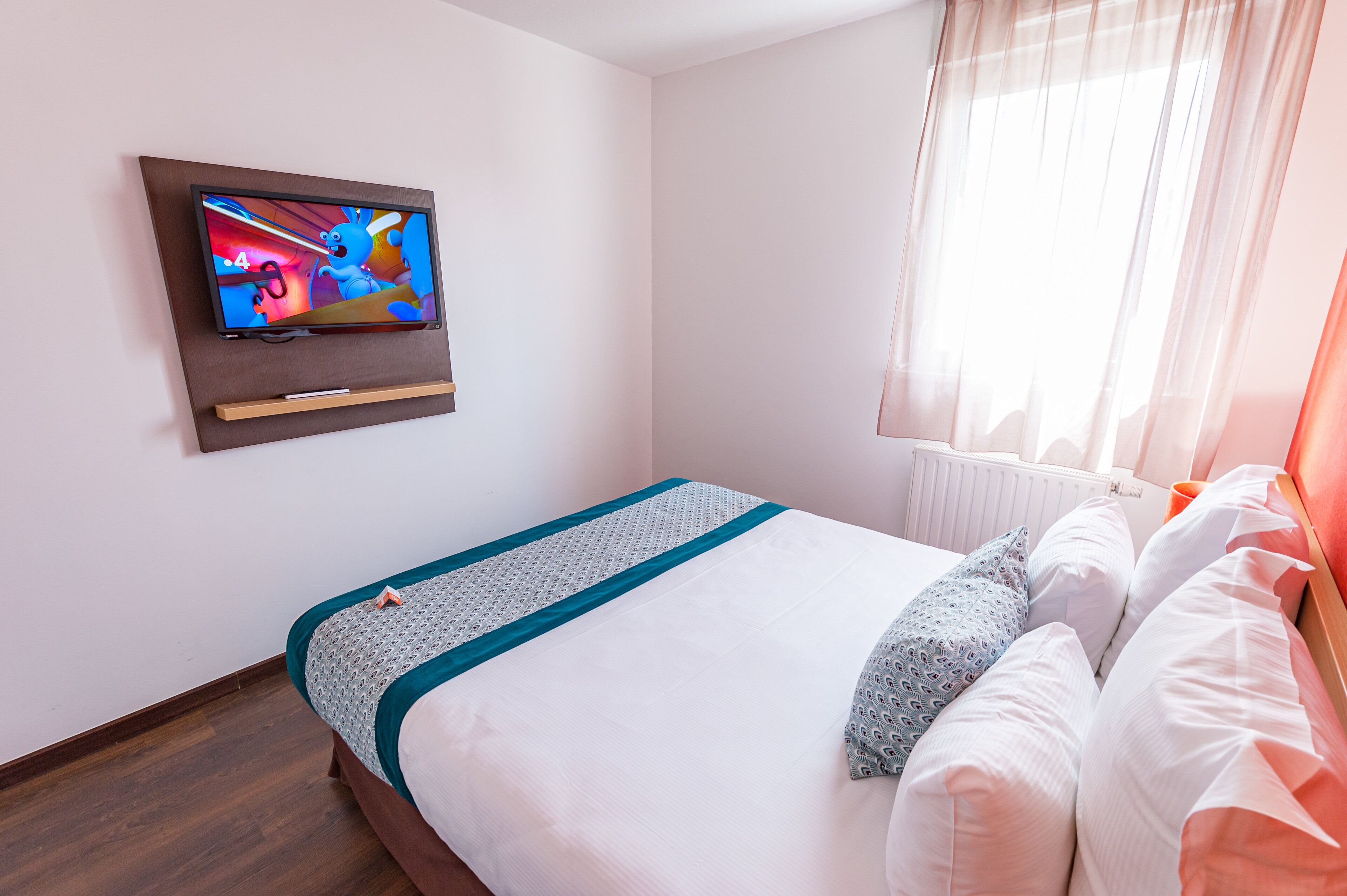 A hotel room with a bed, a TV mounted on the wall, and a window with curtains.
