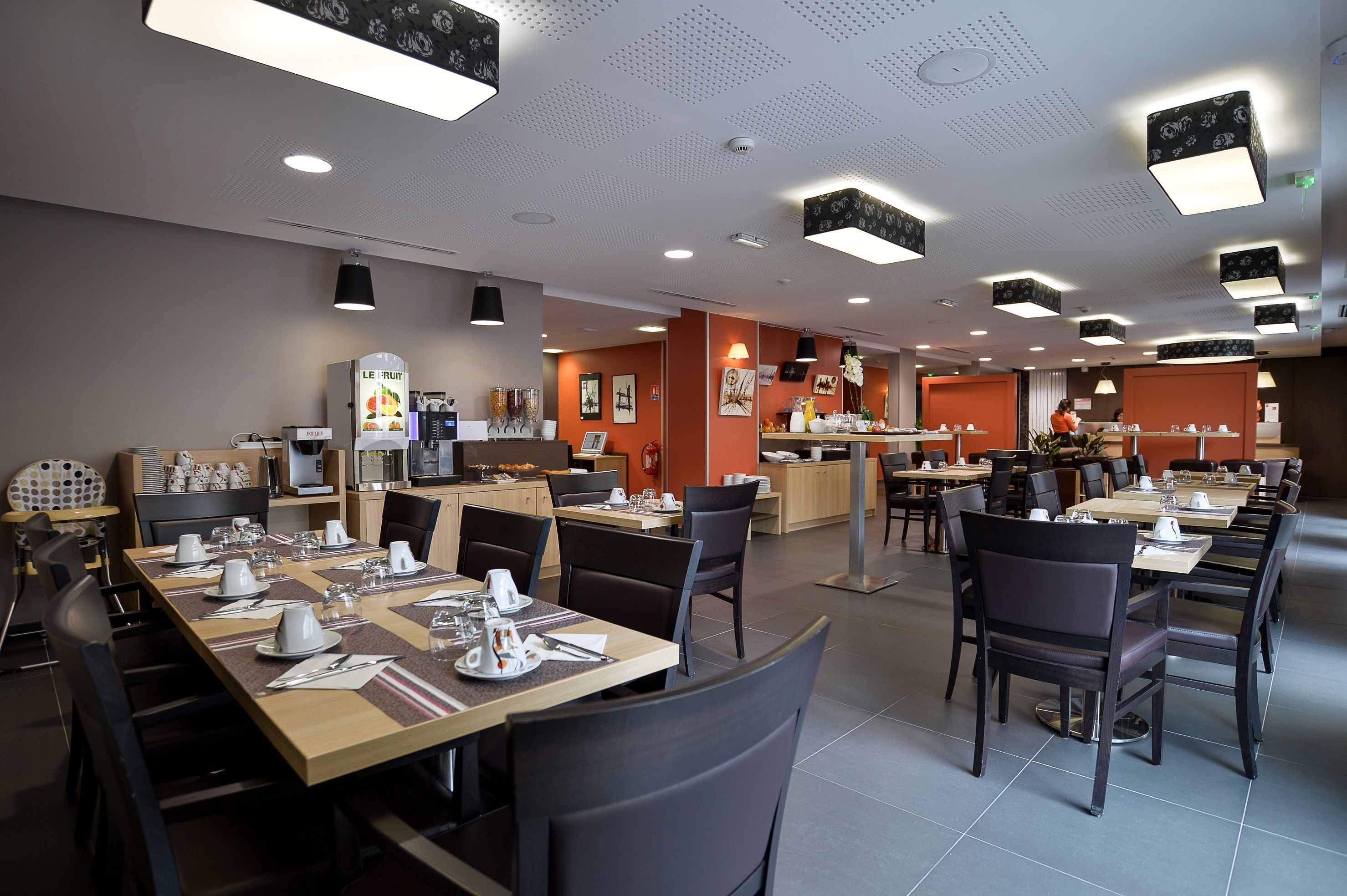 Ein modernes Restaurant mit mehreren Essbereichen, einer Küche im Hintergrund und einer Obstauslage.