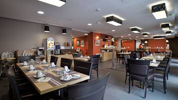 A modern restaurant with multiple dining areas, a kitchen in the background, and a fruit display.