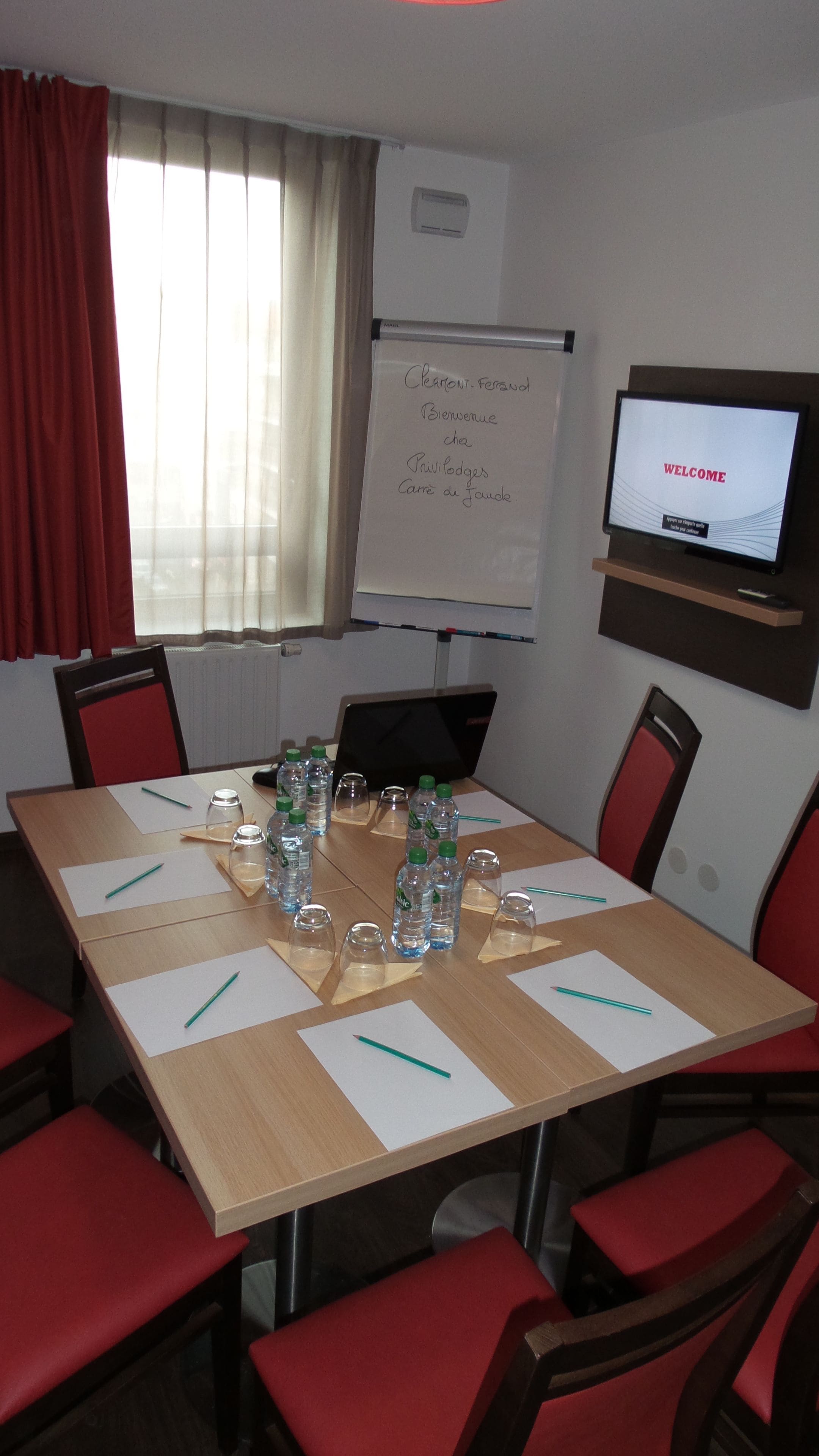 A conference room with a whiteboard, a TV screen displaying 'WELCOME', and a table set with water bottles and notepads.