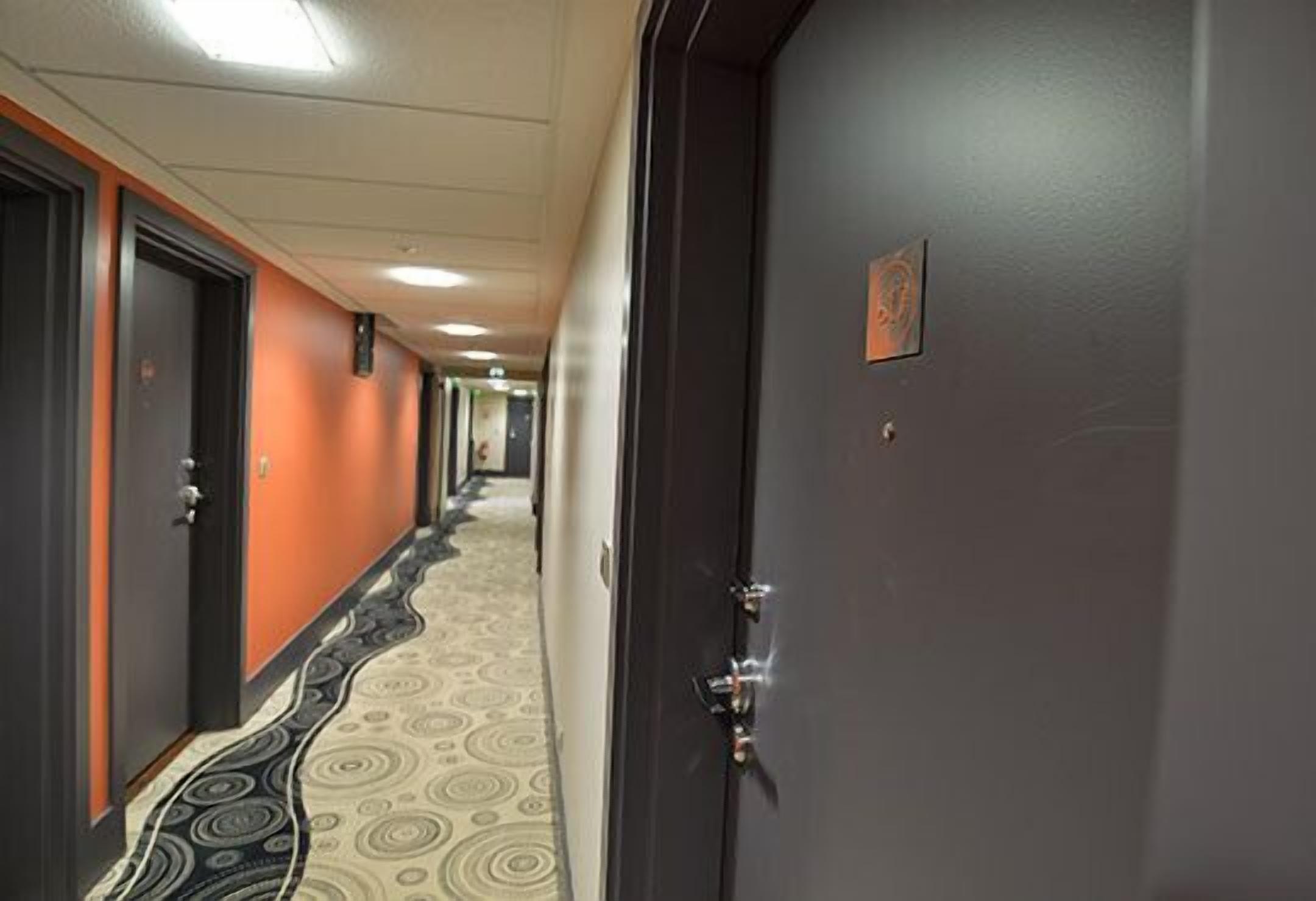 A hotel hallway with patterned carpet, dark doors, and a light-colored wall.