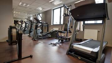 A gym with various exercise machines, large windows, and a tiled ceiling.