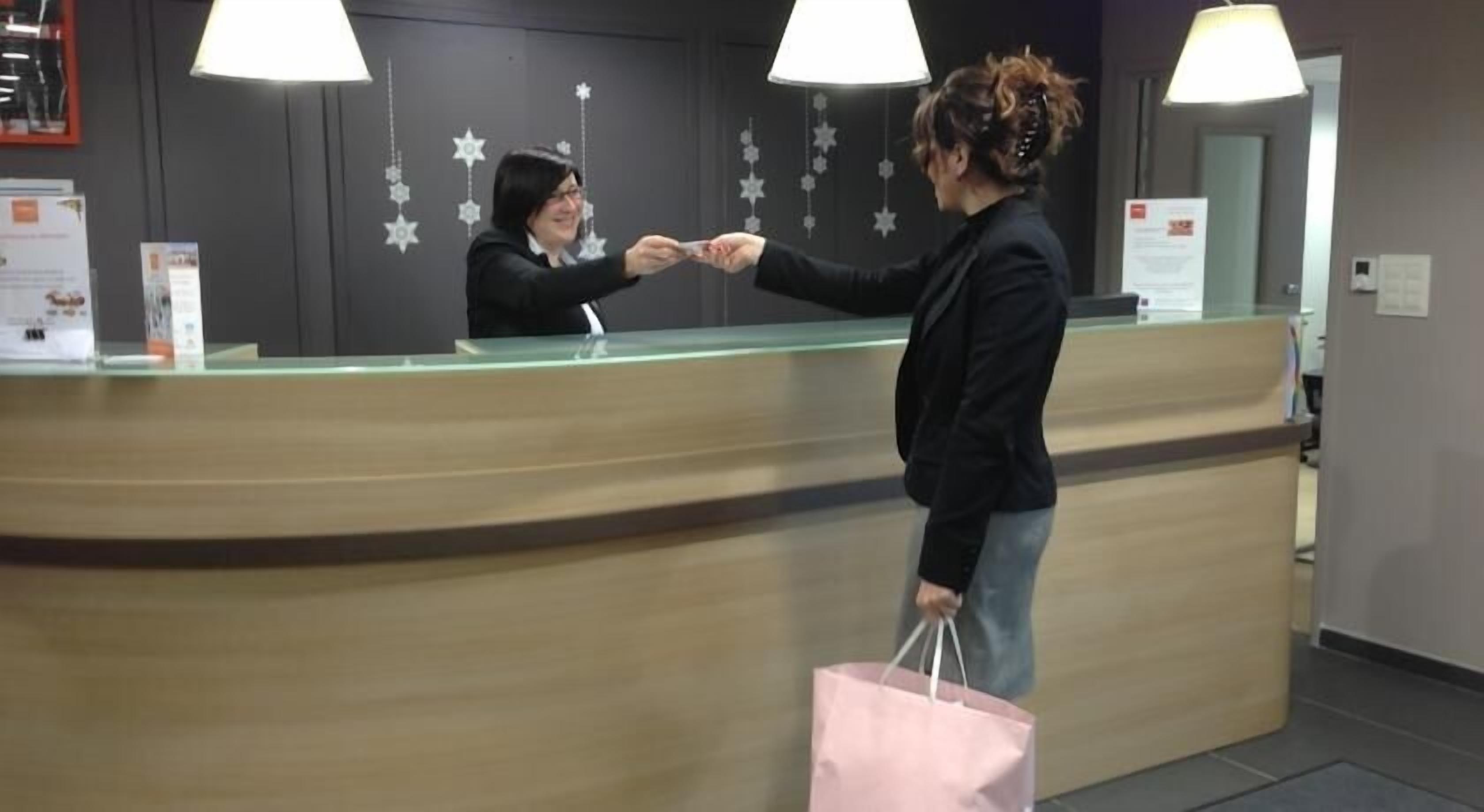 Een receptiebalie met een glazen scheidingswand, decoratieve stervormen aan de muur en een persoon die een kaart aan een receptioniste overhandigt.
