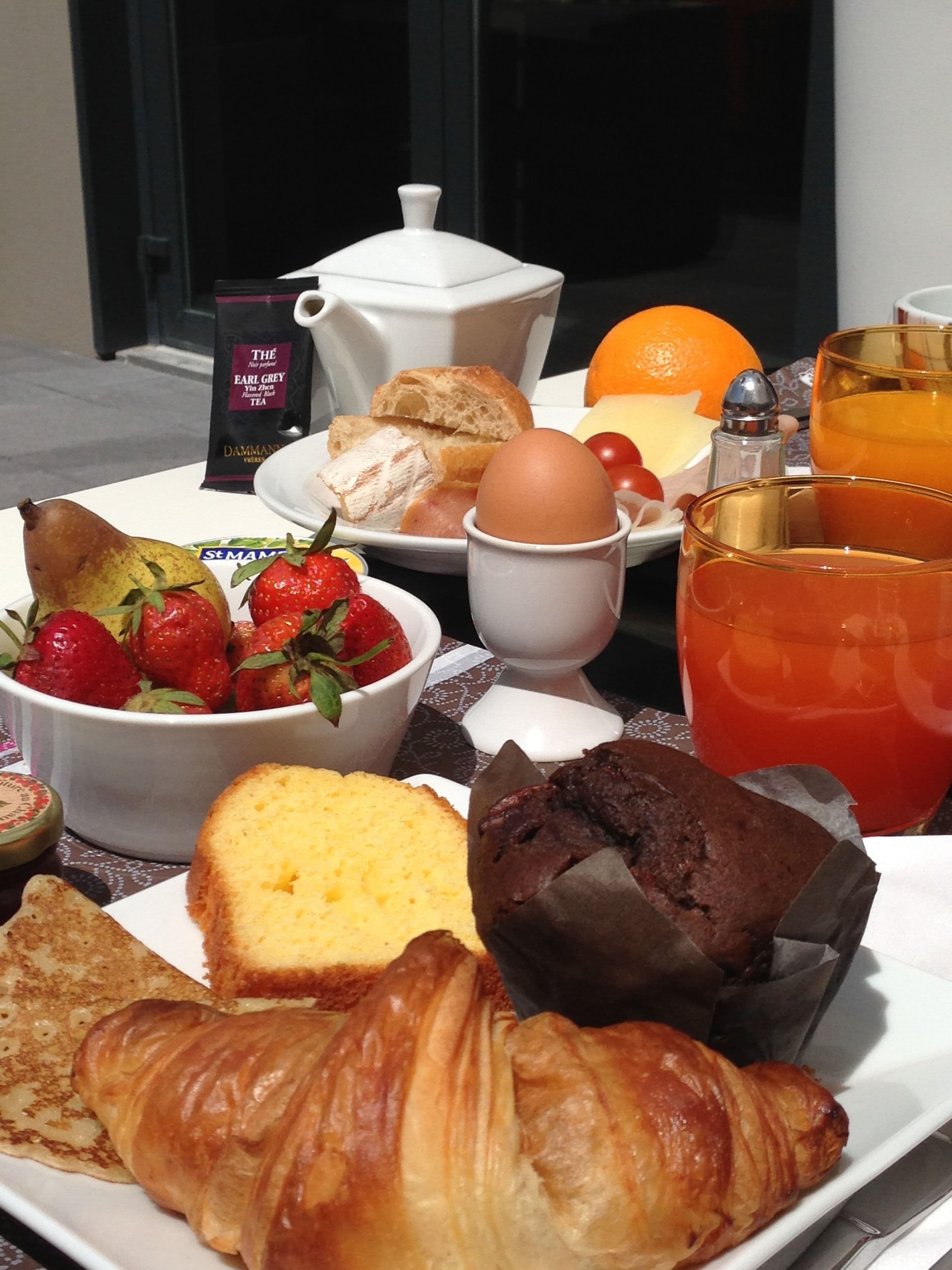 A breakfast tray with bread, eggs, strawberries, a croissant, and a glass of orange juice.