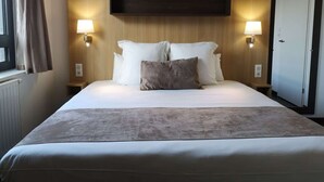 Una habitación de hotel con una cama grande, dos lámparas de noche, un cabecero de madera y una puerta.