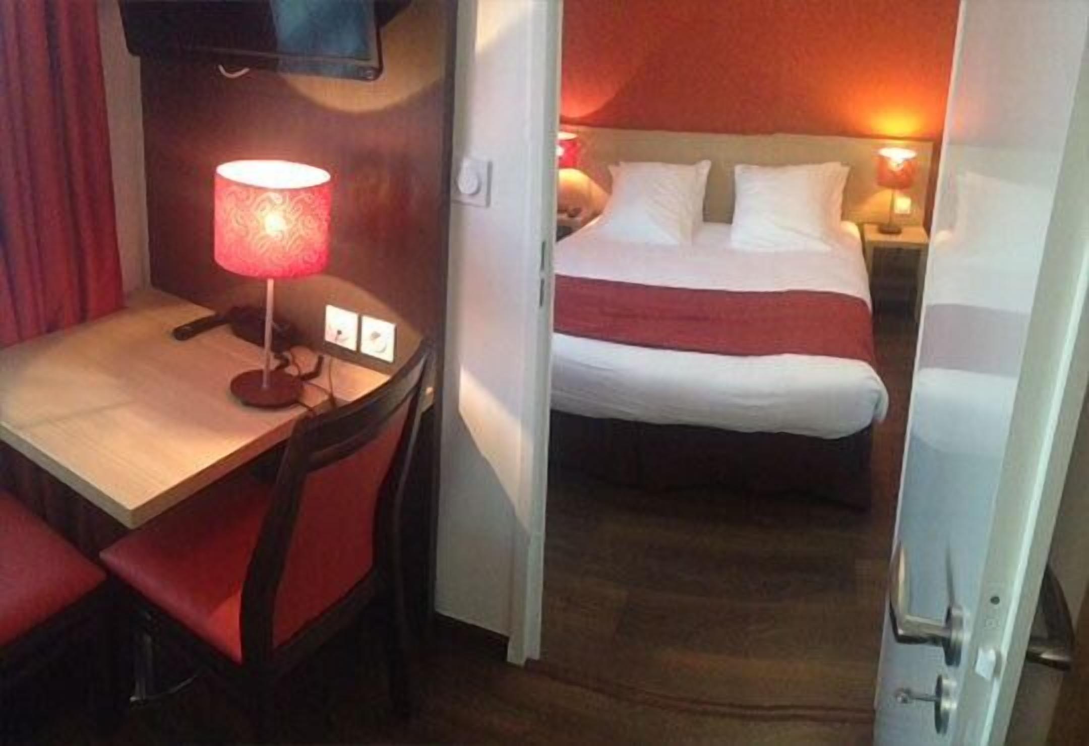 Una habitación de hotel con cama, escritorio con lámpara y televisión en la pared.