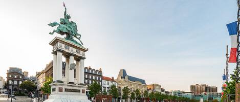 A plaza with a central statue, surrounded by historic buildings and a clear sky.