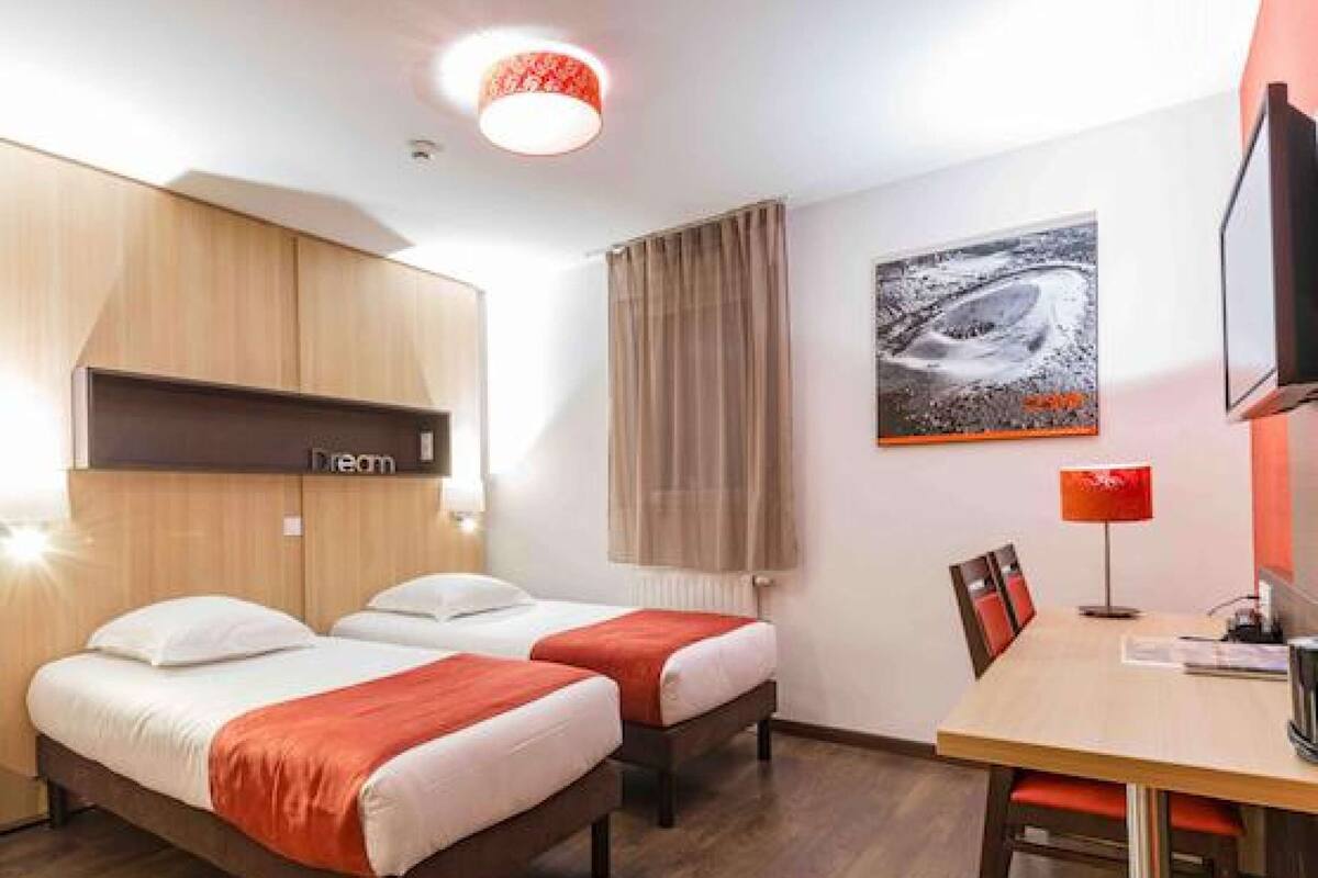 Una habitación de hotel con dos camas, un escritorio, una silla, un televisor y un cuadro en la pared.