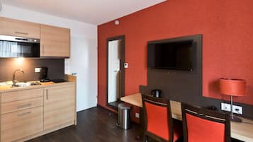 Une cuisine compacte comprenant un évier, une cuisinière et des placards, un coin repas avec une table et des chaises, et un mur d’accent de couleur rouge.