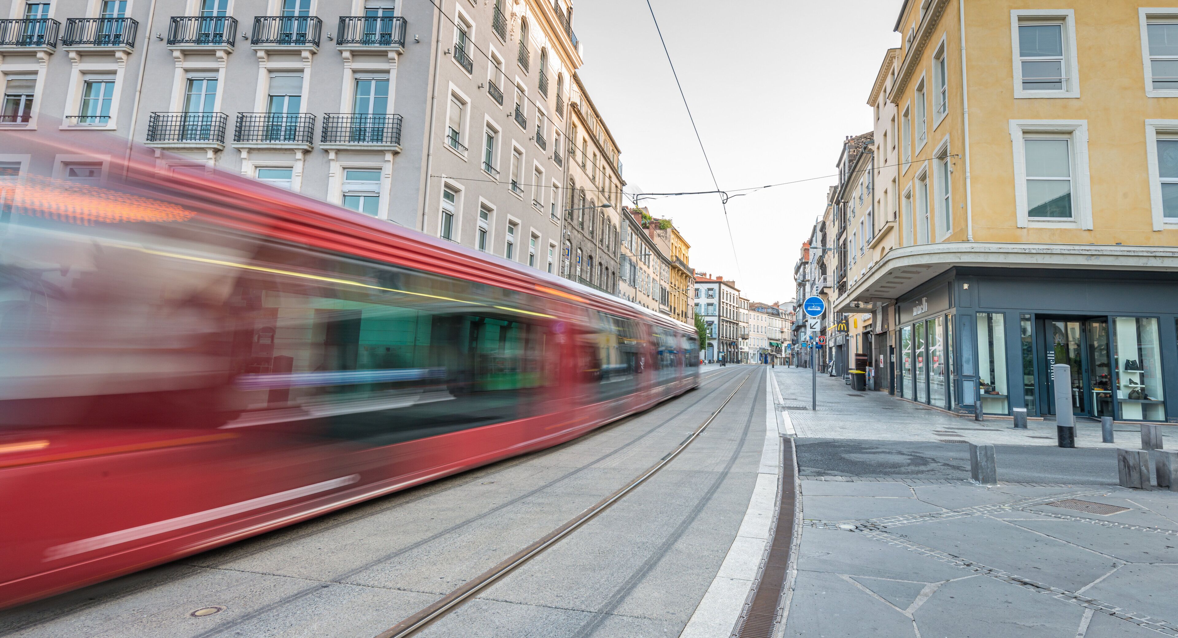 A tram moving along a tram track in a city street with buildings on either side.