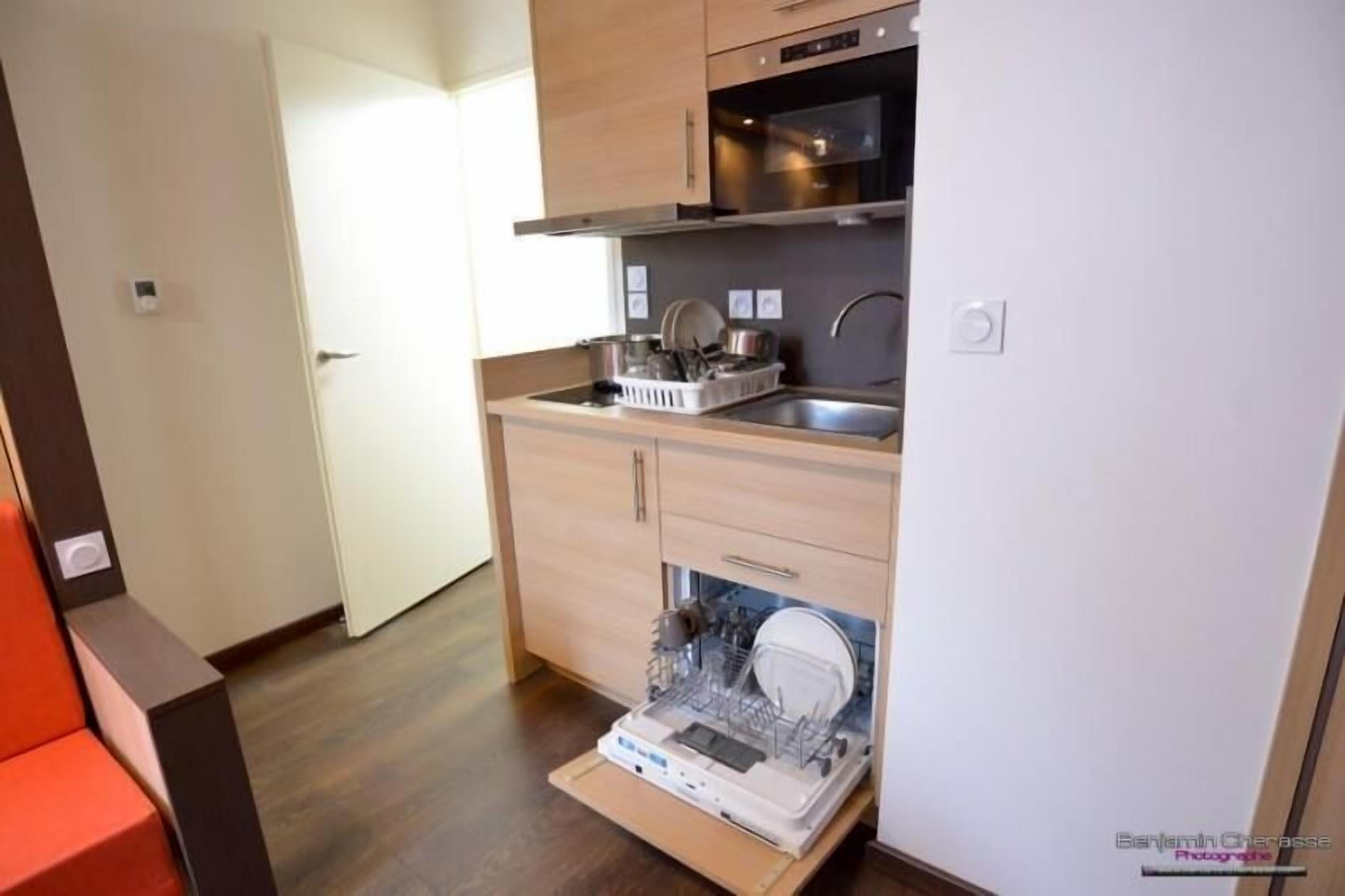 A compact kitchen with wooden cabinets, a stainless steel sink, and a dishwasher.