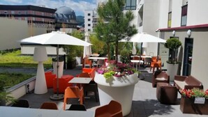 Un patio al aire libre con mesas, sillas, sombrillas y plantas en macetas.