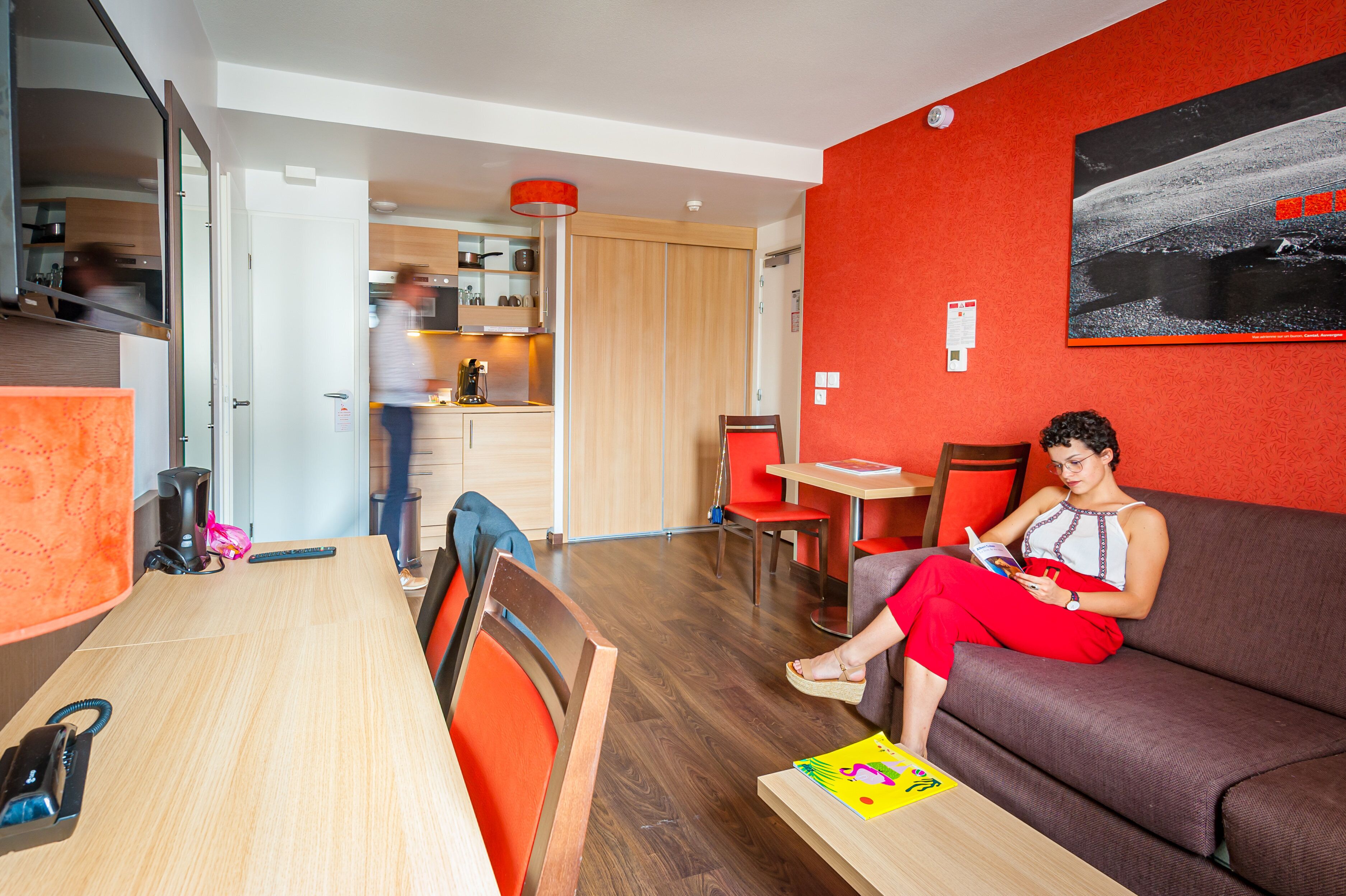 A modern living room with a sofa, a dining table, and a kitchen area in the background.