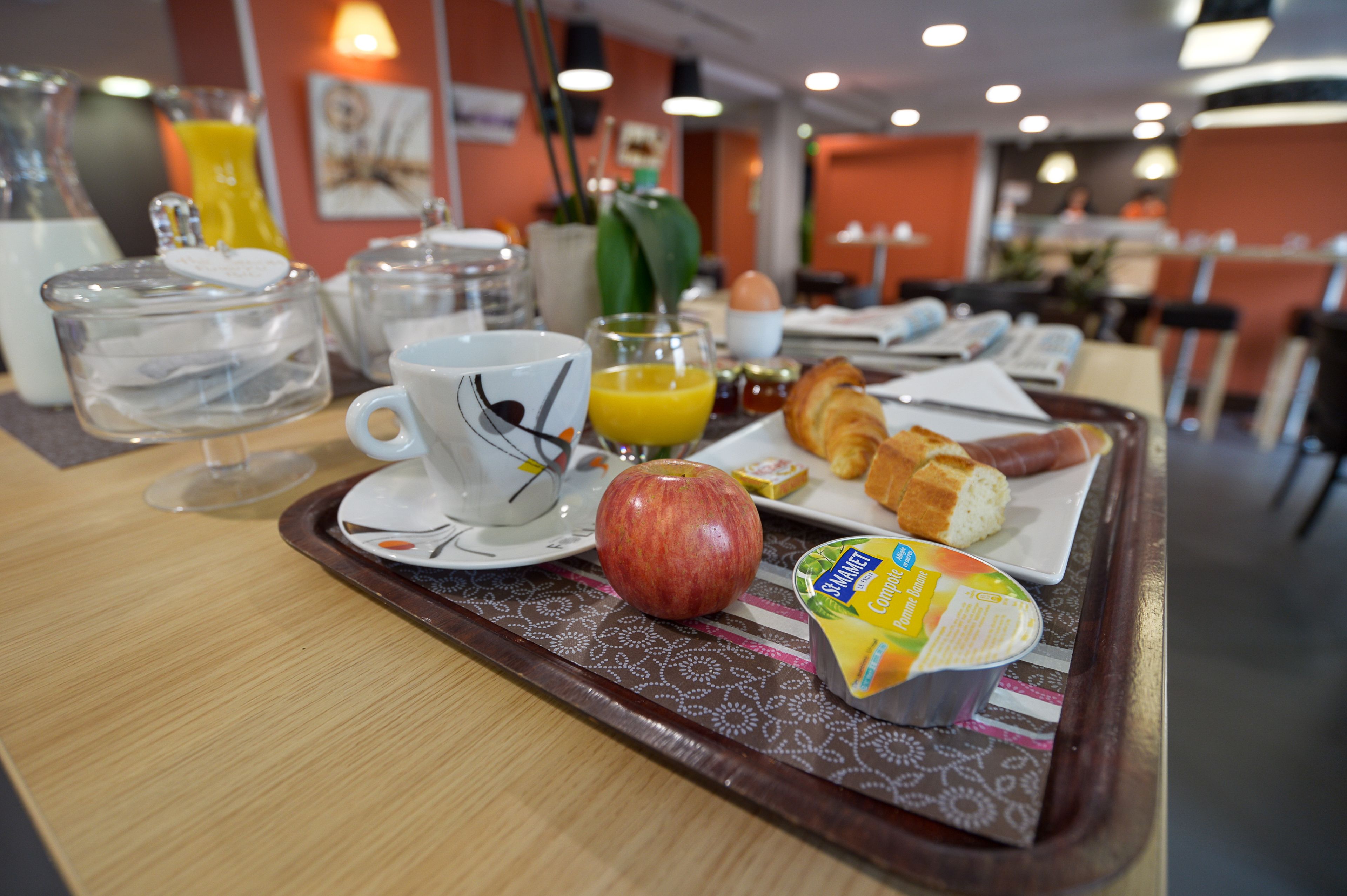 A breakfast tray with a croissant, apple, juice, and yogurt parfait.