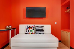 Una habitación con una cama blanca, un televisor de pantalla plana montado en la pared y una pared de acento roja.