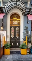 A hotel entrance with a "WELCOME HOME" sign, a black double door with decorative glass panels, and two potted plants on either side.