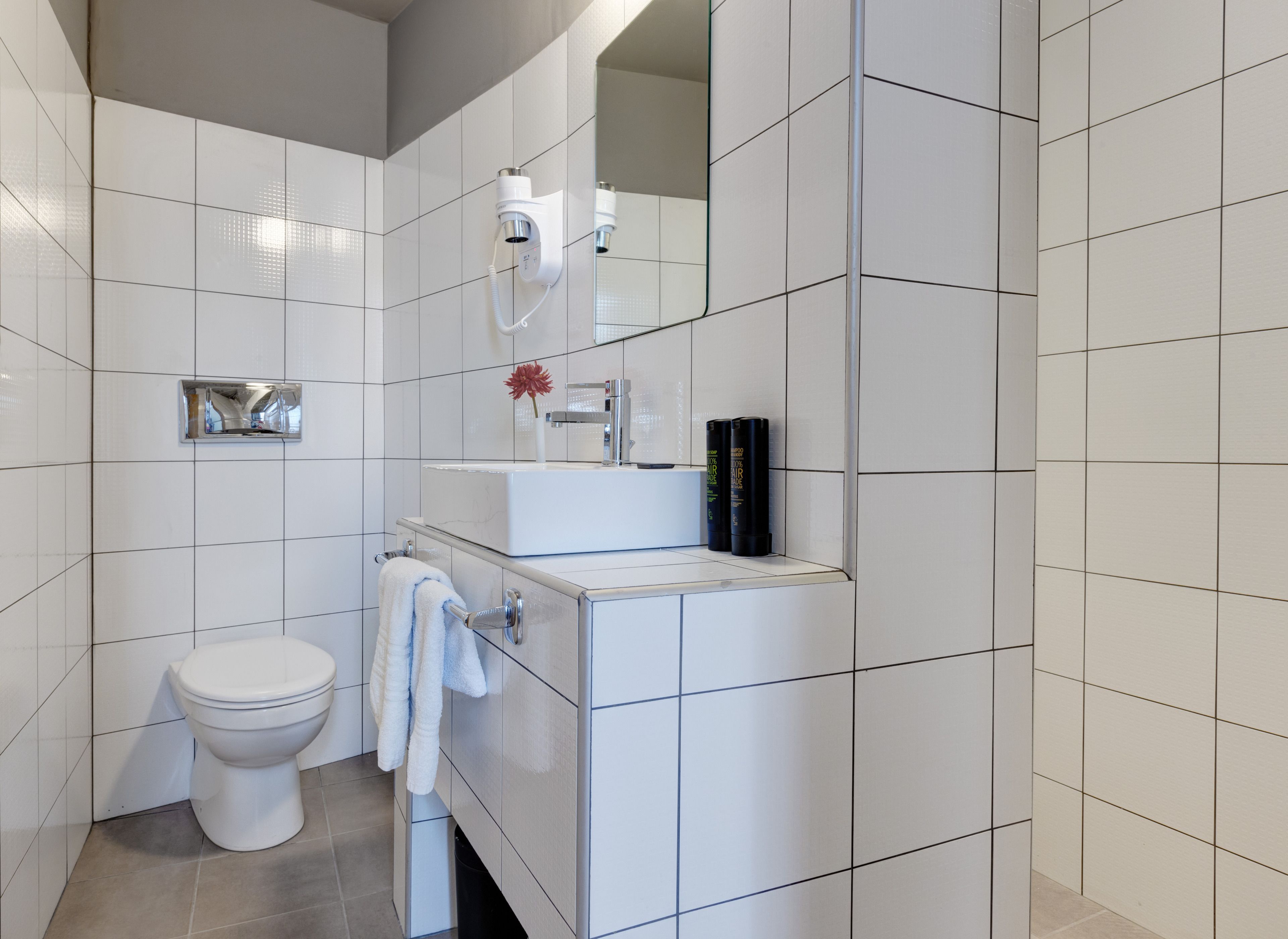 A modern bathroom with white tiles, a toilet, a sink with a mirror, and a hairdryer.