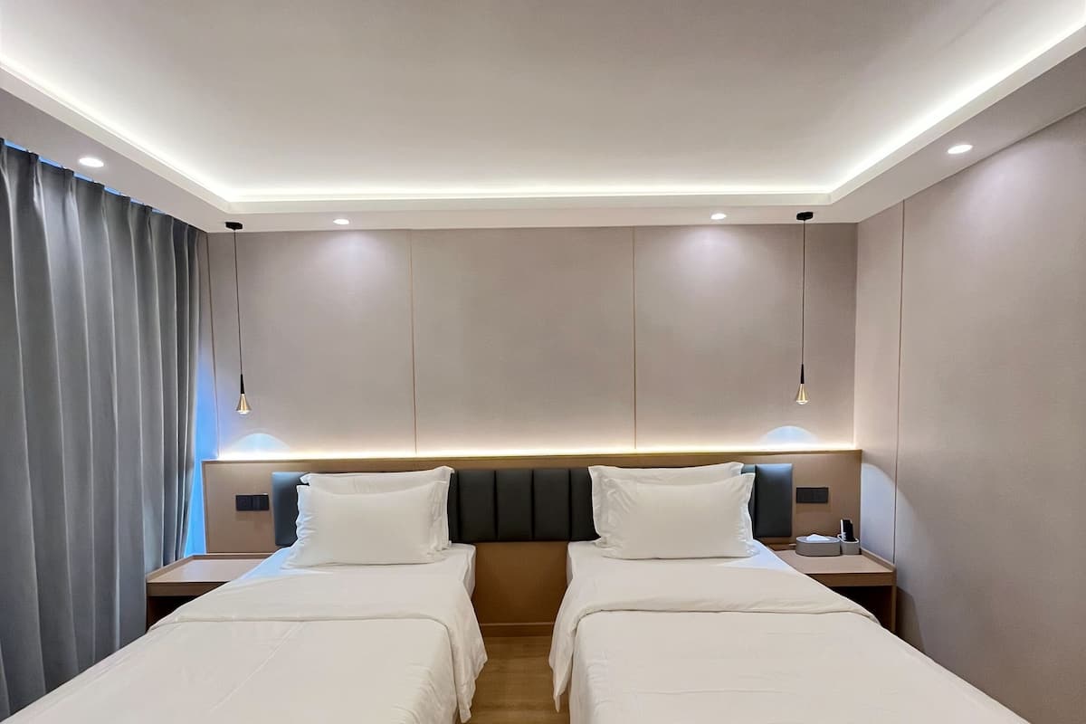A hotel room with two beds, a headboard, bedside tables, and a curtain.
