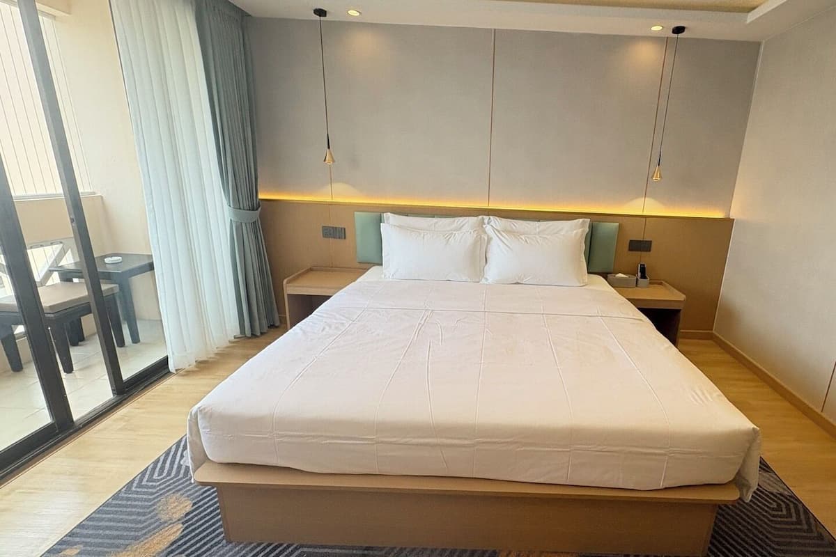 A hotel room with a large bed, a bedside table, a nightstand, and a view through a glass door.