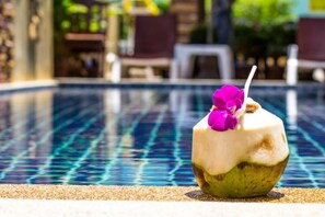 A coconut drink with a straw and purple flower on a poolside. - Hathai House Resort (Koh Samui)