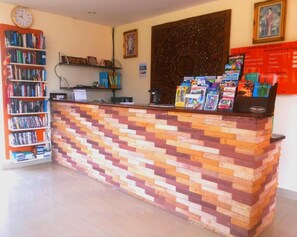 A reception desk with a colorful brick pattern, a clock, and a bookshelf filled with books. - Hathai House Resort (Koh Samui)