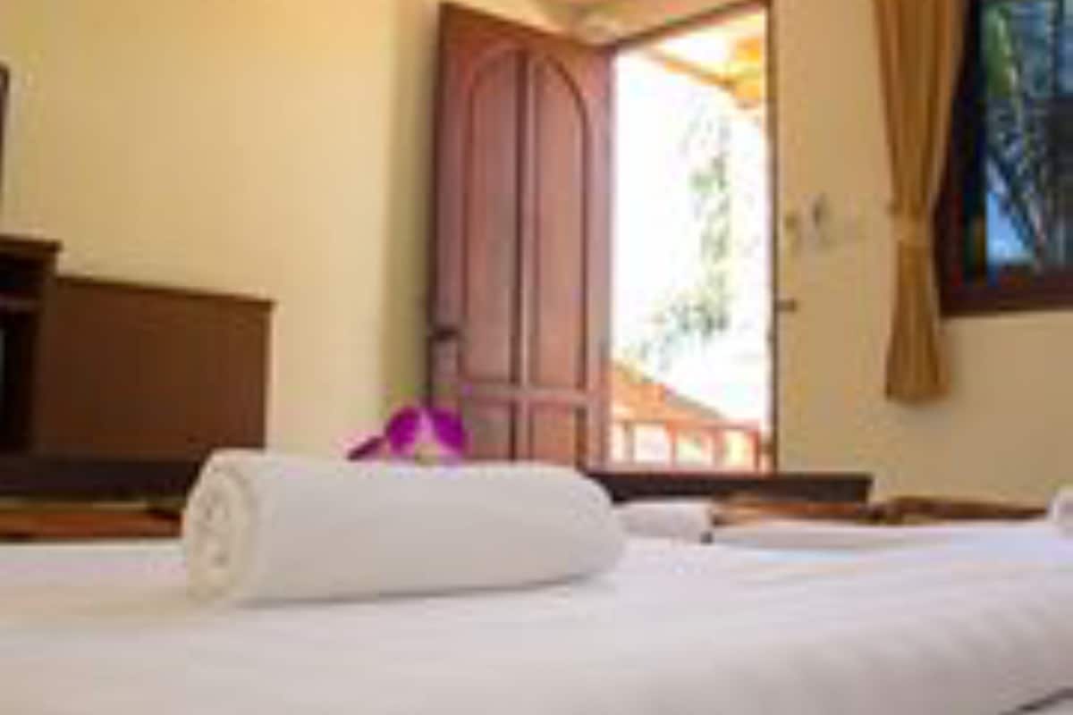 A hotel room with a bed, a wooden door, and a window with curtains.