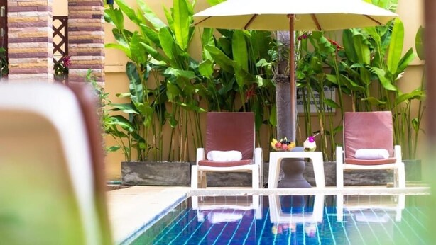 Un área de piscina con dos sillas de descanso y una sombrilla.