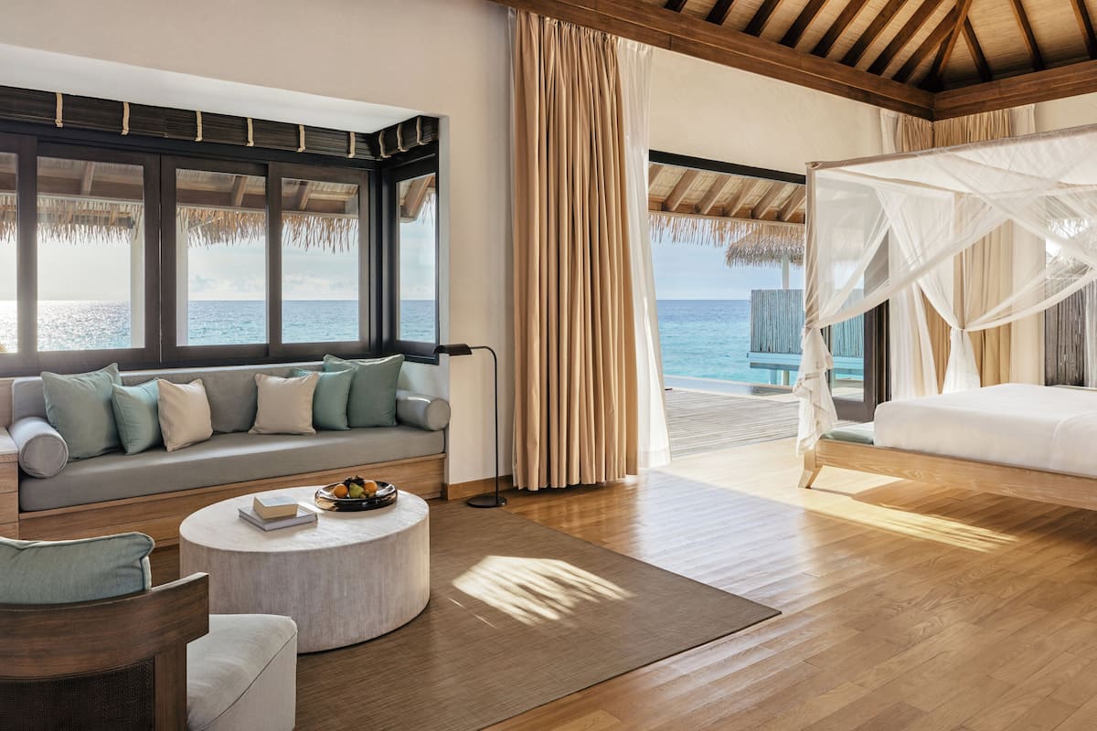 Una habitación de hotel moderna con un ventanal grande, un sofá, una cama con dosel y una mesa de centro redonda.