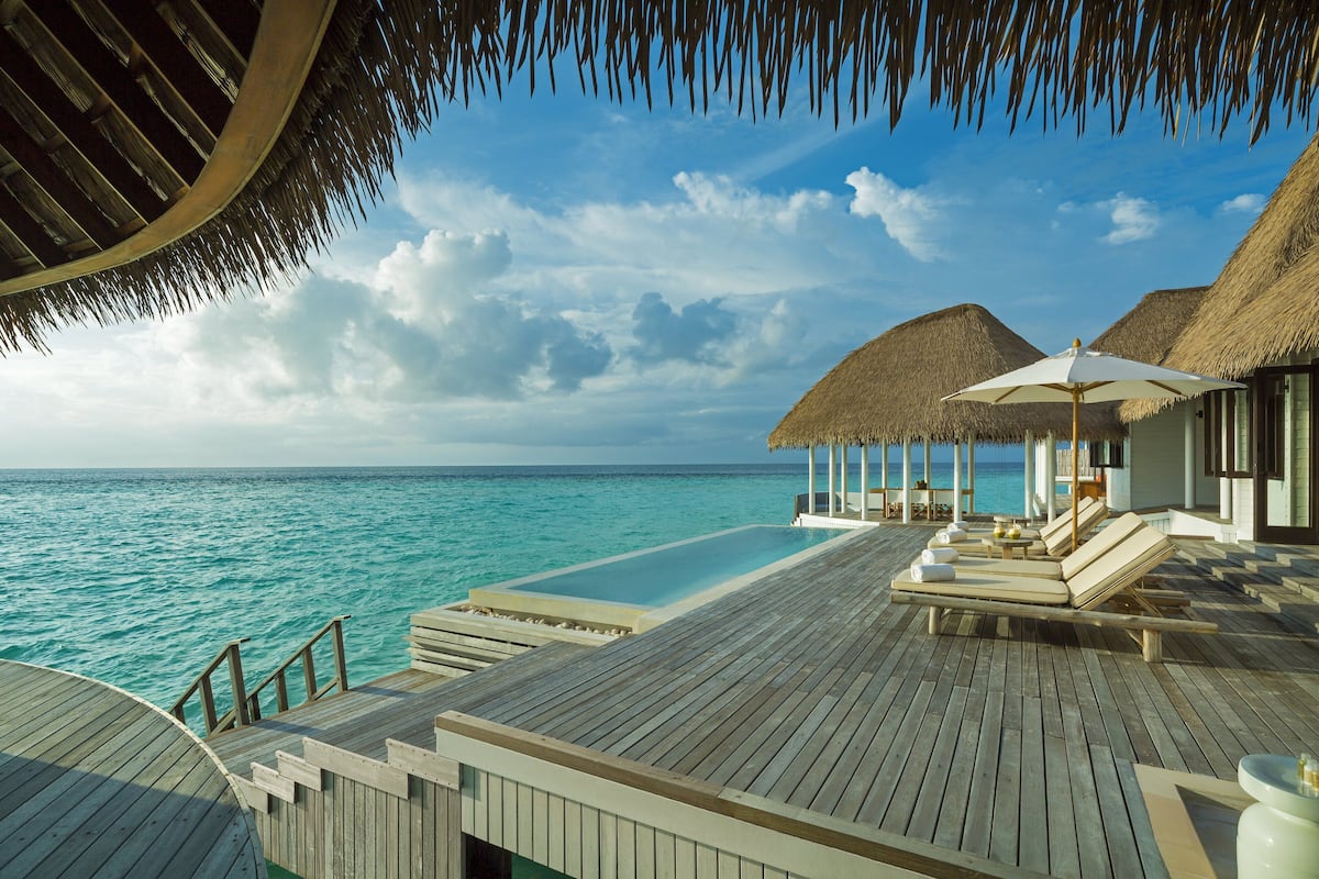 Bungalows sobre el agua con una terraza de madera, sillas de descanso y una piscina con vistas al océano.
