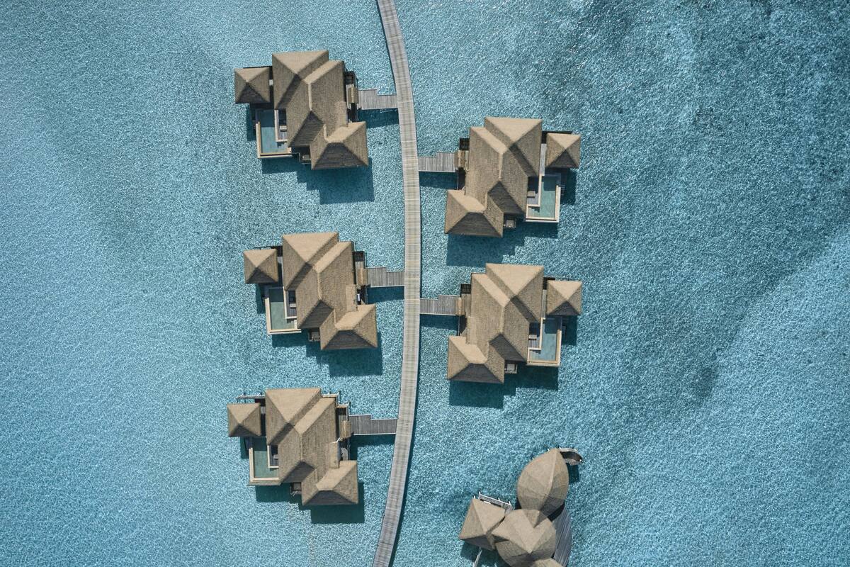 Vista aérea de un resort con bungalows sobre el agua, unidos por una pasarela de madera.