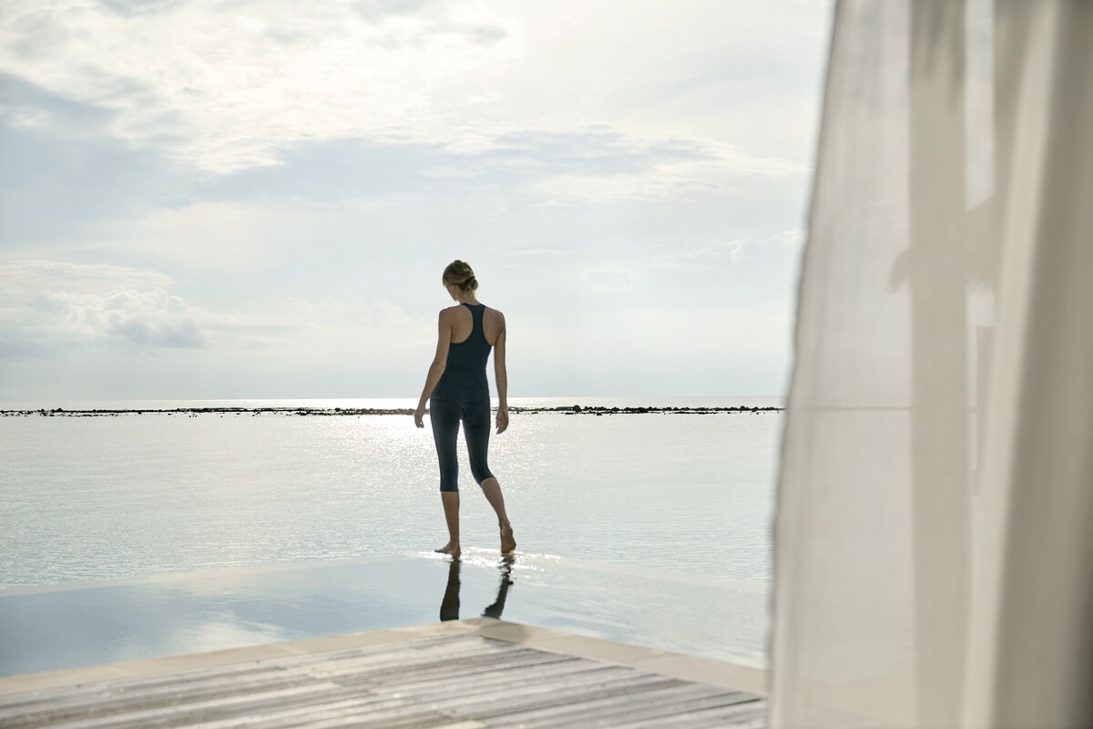 A person standing at the edge of a pool with a view of the sea and a distant shoreline.