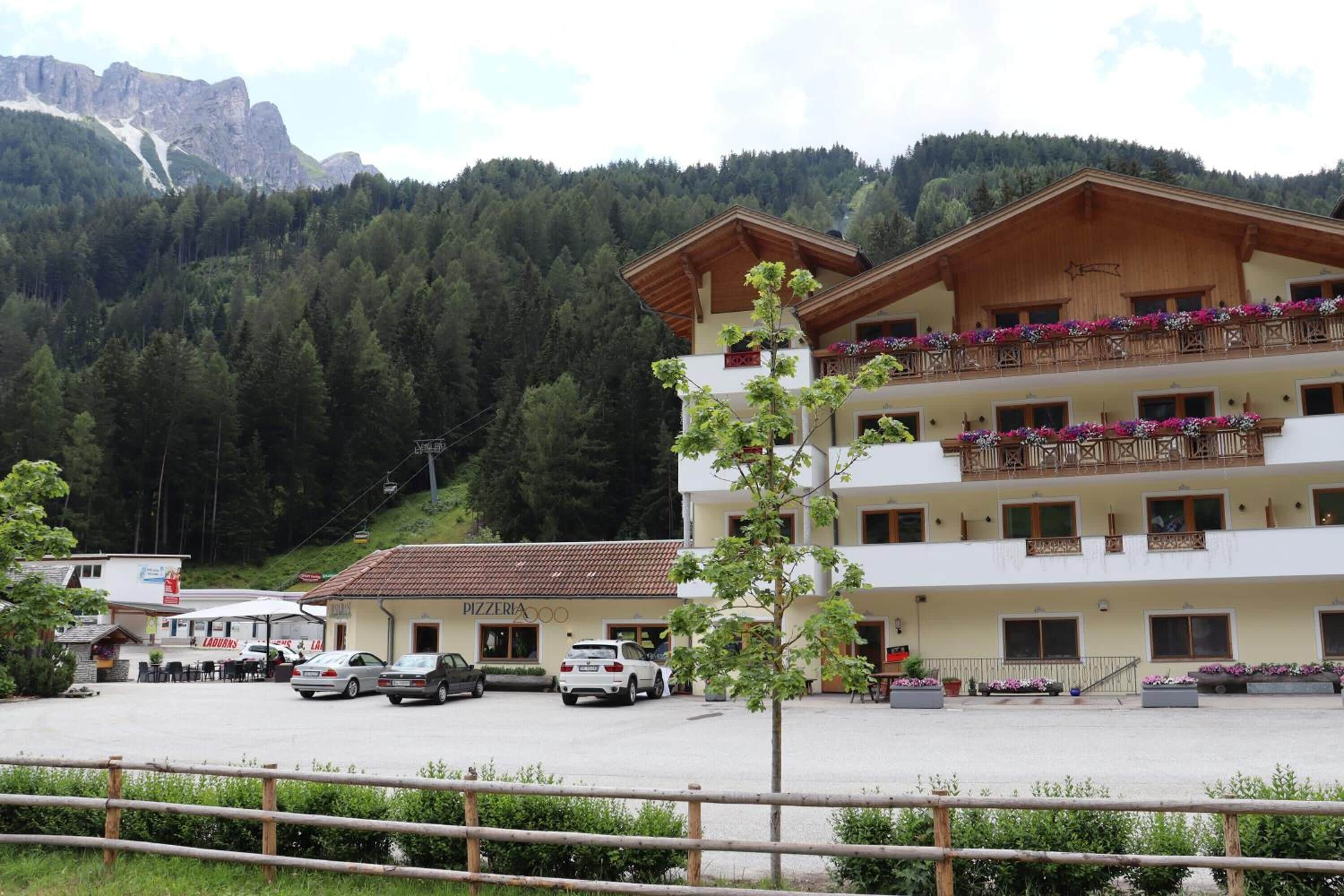Un hotel con fachada blanca, varios balcones con jardineras de flores y un estacionamiento con coches.