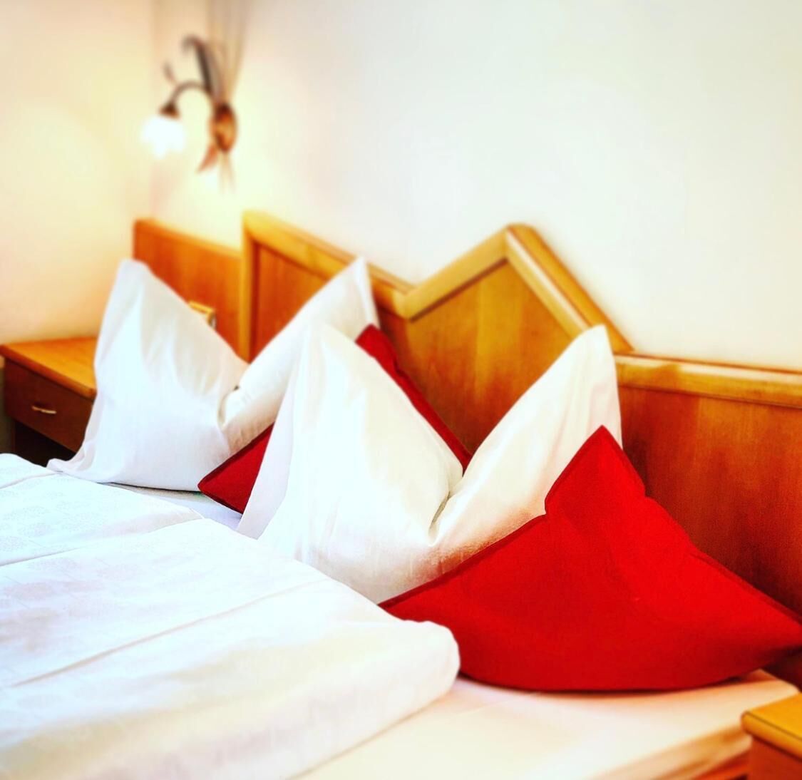 Una cama bien tendida con almohadas blancas y rojas, un cabecero de madera y una mesita de noche.