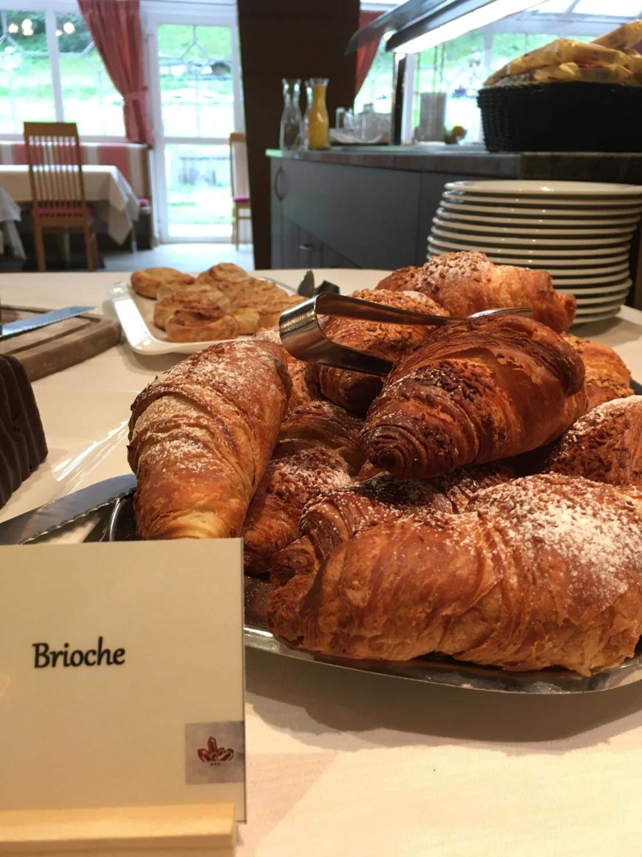 Ein Frühstücksbuffet mit einer Auswahl an Backwaren, darunter Croissants, und einem Schild mit der Aufschrift 'Brioche'.