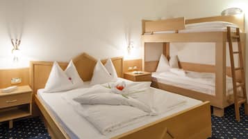 A hotel room with a bunk bed, a single bed, a bedside table with a lamp, and a small desk with a chair.