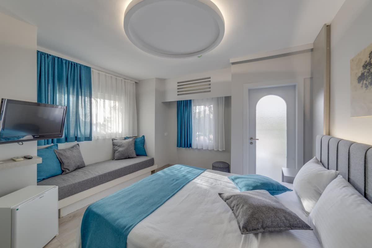 A modern hotel room with a bed, a TV, a seating area, and a door leading to a balcony.