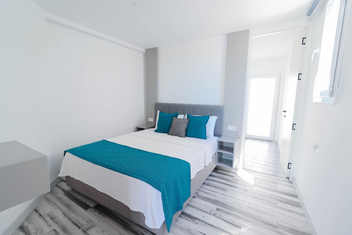 A modern bedroom with a bed, nightstands, and a hallway leading to a door.