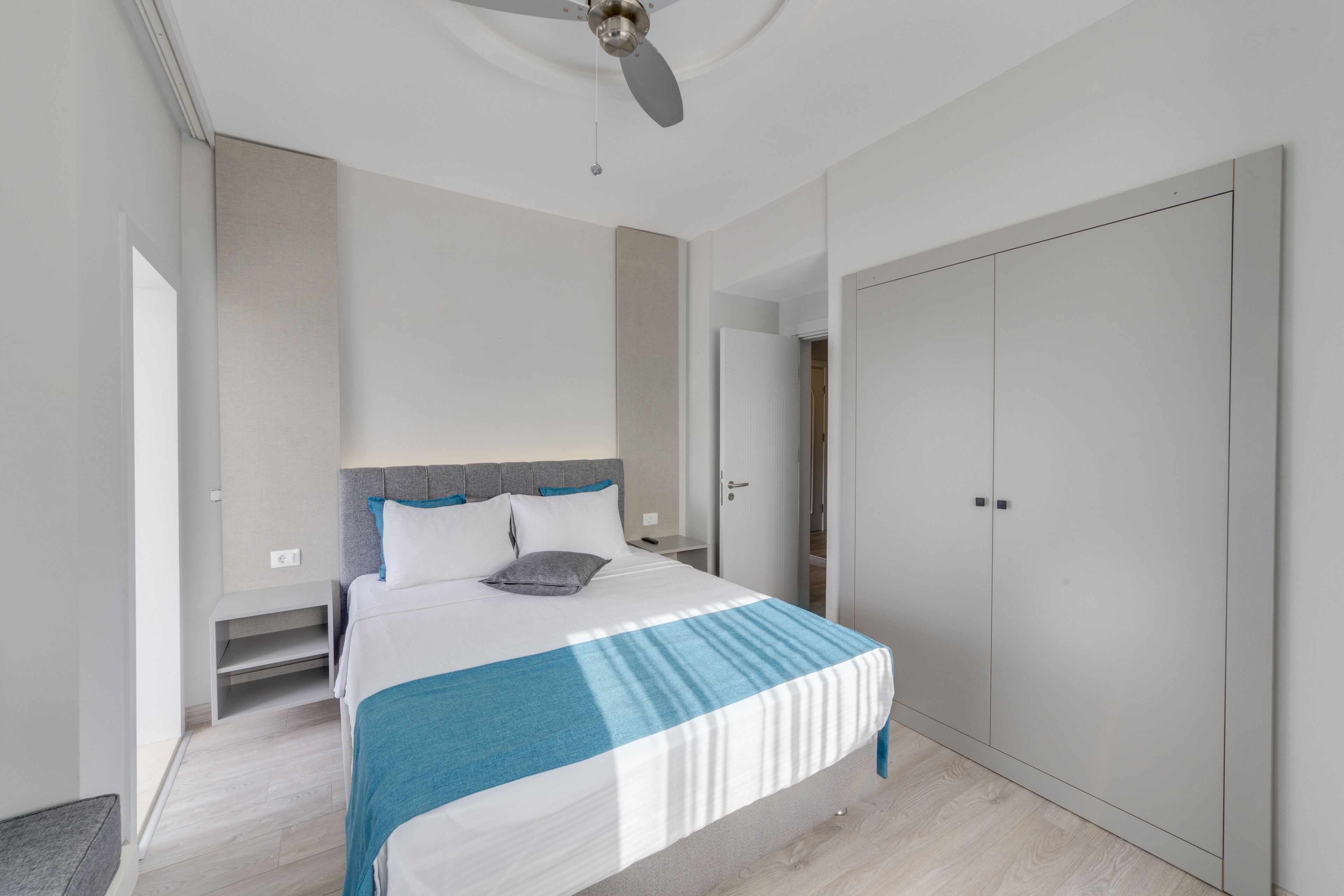 A modern bedroom with a bed, a ceiling fan, a wardrobe, and a nightstand.