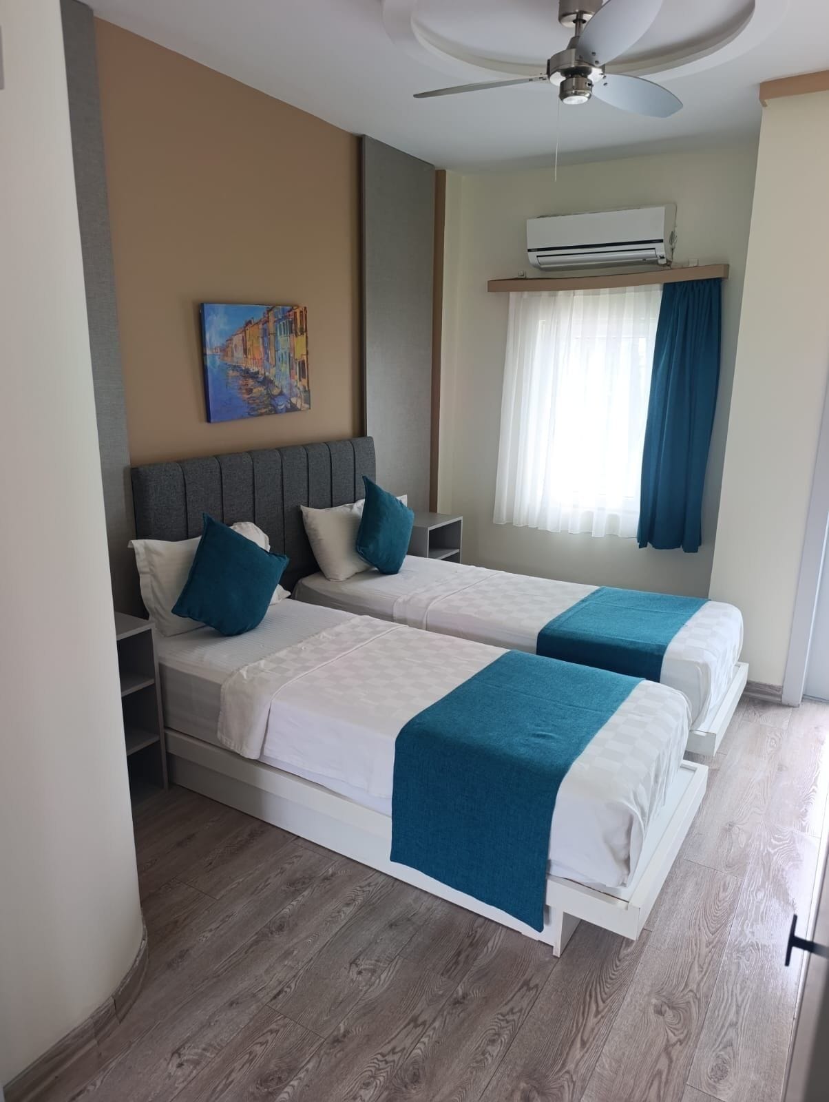 Een hotelkamer met twee bedden, een plafondventilator, een airconditioningsysteem en een schilderij aan de muur.