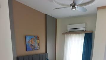 A hotel room with two beds, a ceiling fan, an air conditioning unit, and a painting on the wall.